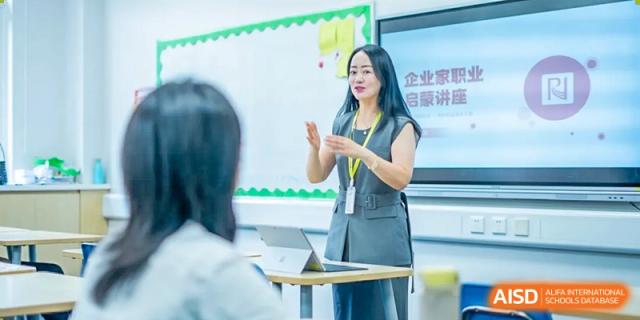 A female teacher using hand gestures while leading a discussion or lesson in a modern classroom at Hiba Academy Hangzhou.