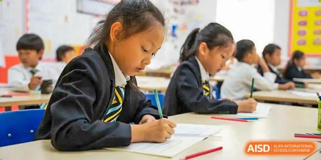 A young female student in uniform focused on writing notes or completing a task at her desk in a classroom at Hiba Academy Hangzhou.