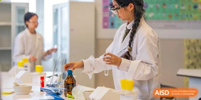 A female student wearing a white lab coat and glasses carefully pouring liquid from a bottle during a chemistry lab session at Hiba Academy Hangzhou.