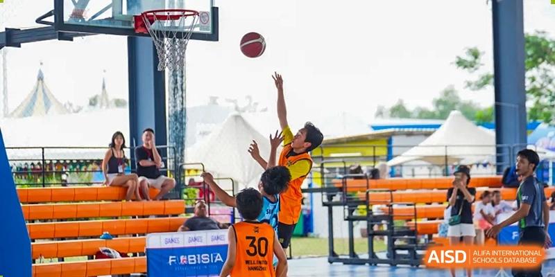 Two students playing basketball outdoors, with one student leaping to catch the ball near the hoop, during a sports event at Hiba Academy Hangzhou.