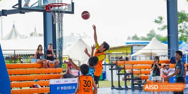 Two students playing basketball outdoors, with one student leaping to catch the ball near the hoop, during a sports event at Hiba Academy Hangzhou.