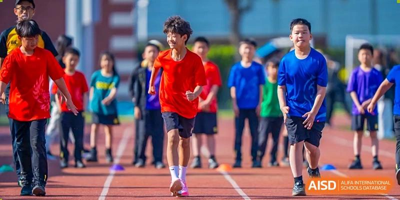 A male student in a red shirt running during a track and field event while other students watch in the background at Hiba Academy Hangzhou.