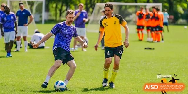 Two men playing soccer on a green field during an outdoor sports event at Hiba Academy Hangzhou.