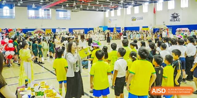 A large group of students in yellow and black shirts attending an indoor school assembly or gathering at Hiba Academy Hangzhou.