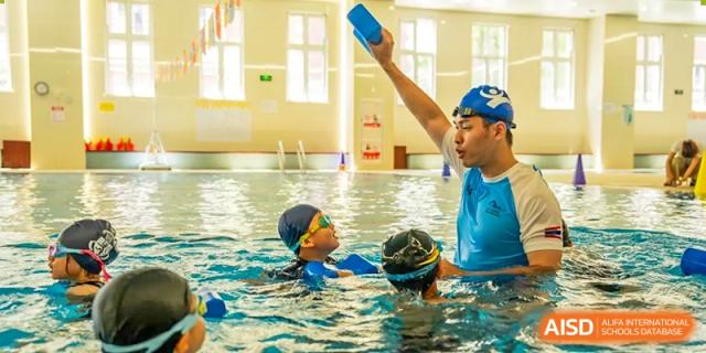 A swimming instructor wearing a blue cap teaching a student in the pool during a lesson at Hiba Academy Hangzhou.