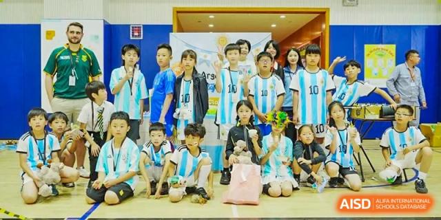 A group of children in light blue and white soccer jerseys posing with small prizes after a competition at Hiba Academy Hangzhou.