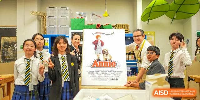 Two students and an adult posing with a movie poster for the production Annie at Hiba Academy Hangzhou.