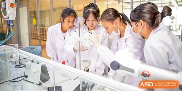 Students in lab coats and safety goggles performing a chemistry experiment with beakers and test tubes at Huitong School & Studios.