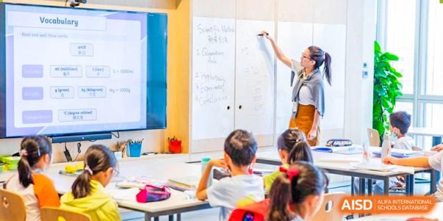 A group of students sitting at desks, facing a whiteboard during a lesson at Huitong School & Studios.