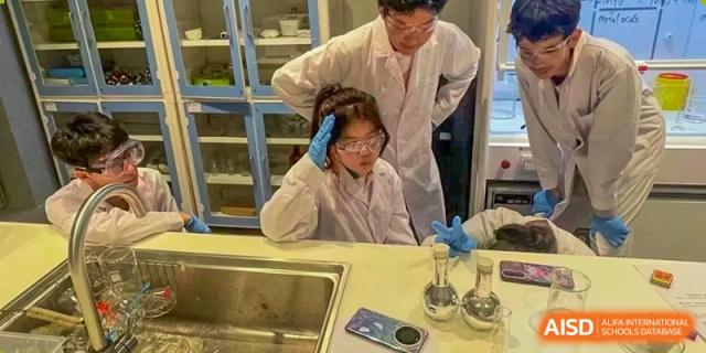 A teacher helping a student in a lab coat and safety goggles with an experiment at a lab table at Huitong School & Studios.