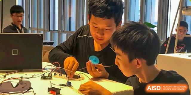 Two students collaborating on a hands-on project with wires and a circuit board at Huitong School & Studios.