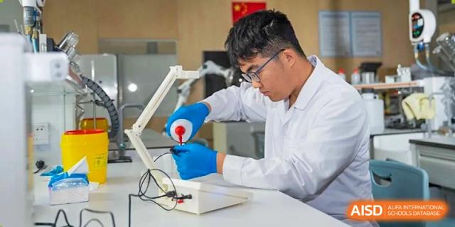 A student in a lab coat and blue gloves carefully using a dropper to add liquid to a project at Huitong School & Studios.