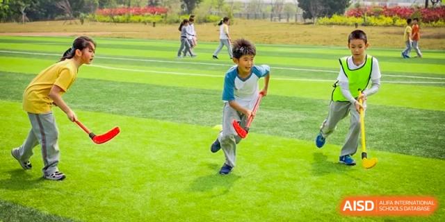 A young boy playing field hockey on a grassy sports field at Huitong School & Studios.