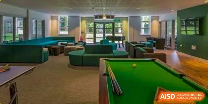 An indoor common area with a billiard table and green seating, providing a space for students to relax at Huitong School & Studios.