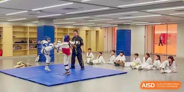 A martial arts instructor working with a student in protective gear while other students watch at Huitong School & Studios.