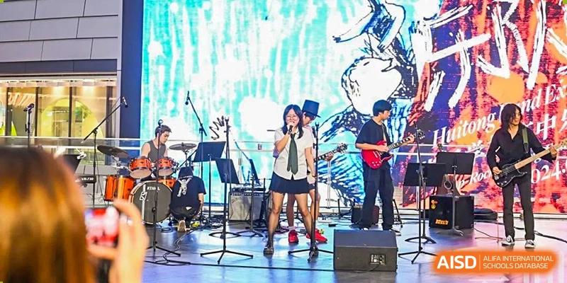 A band of students performing on a stage with a brightly lit background at Huitong School & Studios.