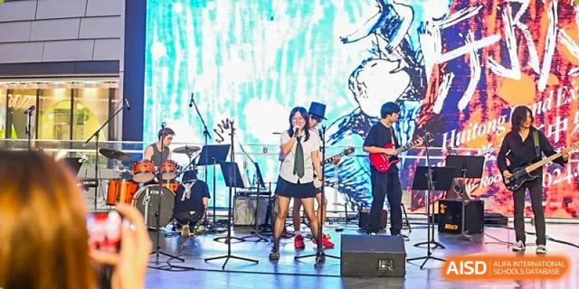 A band of students performing on a stage with a brightly lit background at Huitong School & Studios.