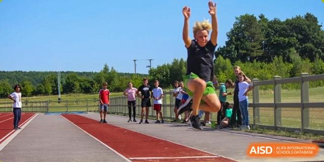 A student participating in a long jump or high jump event on an athletic track at Huitong School & Studios.