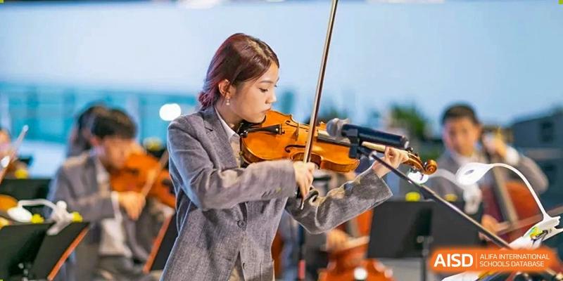 A female student in a formal outfit concentrating while playing the violin at Huitong School & Studios.