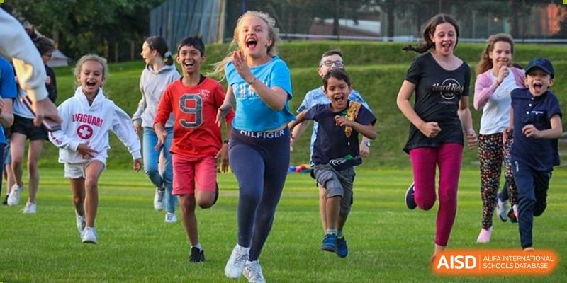 A group of children joyfully running and playing on a grassy field at Huitong School & Studios.