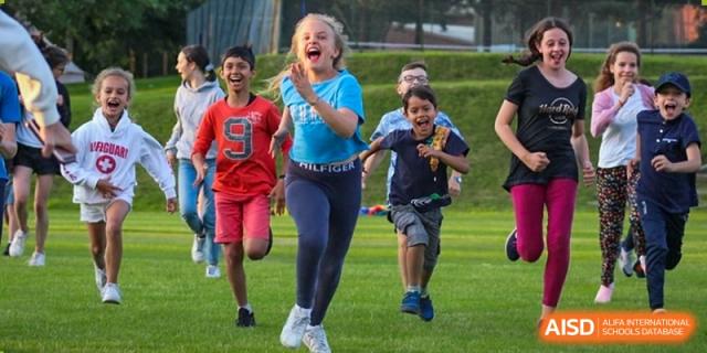 A group of children joyfully running and playing on a grassy field at Huitong School & Studios.