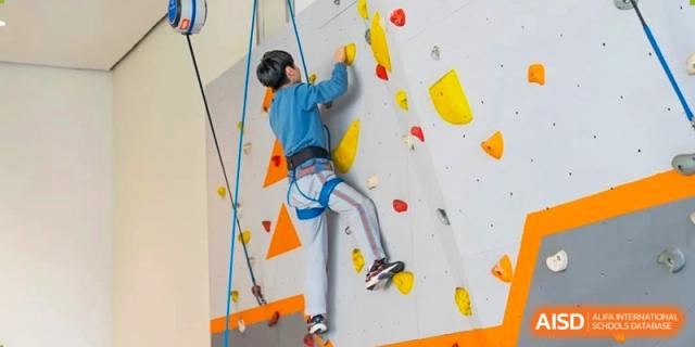 A student carefully climbing a rock wall indoors as part of a physical education class at Huitong School & Studios.