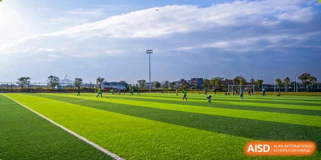 A wide shot of a large, green sports field with students playing in the distance at Huitong School & Studios.