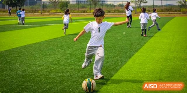 A young boy kicking a soccer ball on a green turf field at Huitong School & Studios.