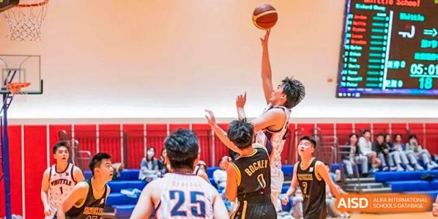 A basketball player in a white jersey shooting a basketball in a gym at Huitong School & Studios.