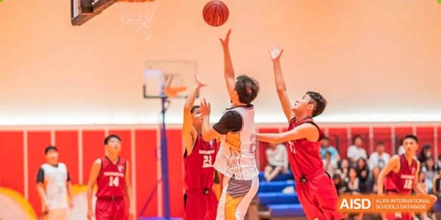 Students playing basketball in a gymnasium, with one player going for a shot at the basket at Huitong School & Studios.