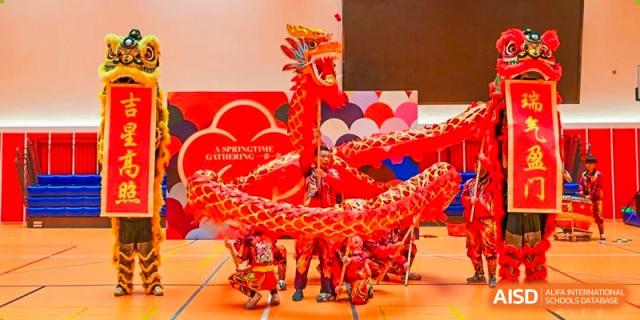 A traditional Chinese dragon dance performance taking place on a stage at a school event at Huitong School & Studios.