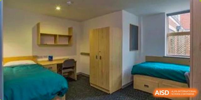 A dormitory room with a bed, desk, and a wooden wardrobe at Huitong School & Studios.