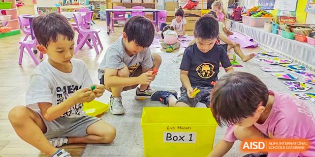 Young students at QSI International School of Zhuhai work together on a hands-on project with materials in a yellow box labeled "Box 1".