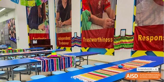 A display area at QSI International School of Zhuhai with books, art supplies, and posters promoting character traits like "Trustworthiness" and "Independent Endeavor".