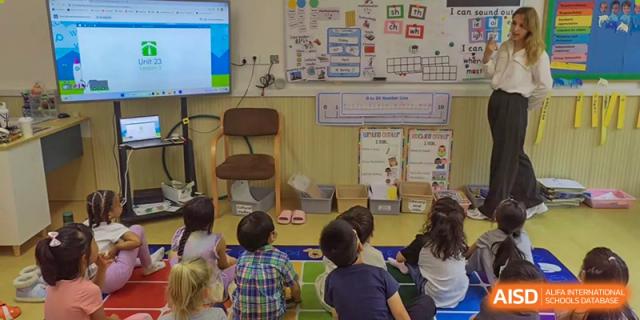 Elementary students at QSI International School of Zhuhai sit on the floor and focus on a presentation or activity led by a teacher.