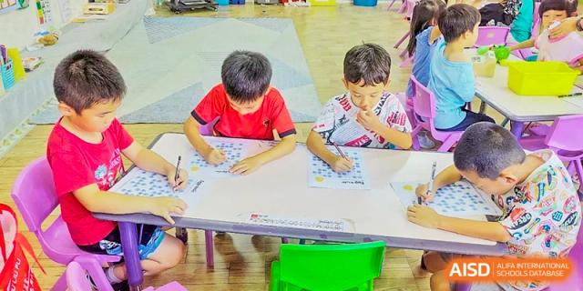 Two young male students at QSI International School of Zhuhai drawing and writing on paper at a small desk.