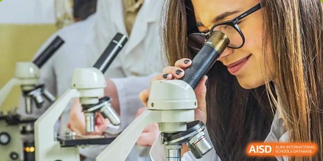 Close-up shot of a student or teacher adjusting the focus on a microscope in a science class at QSI International School of Zhuhai.