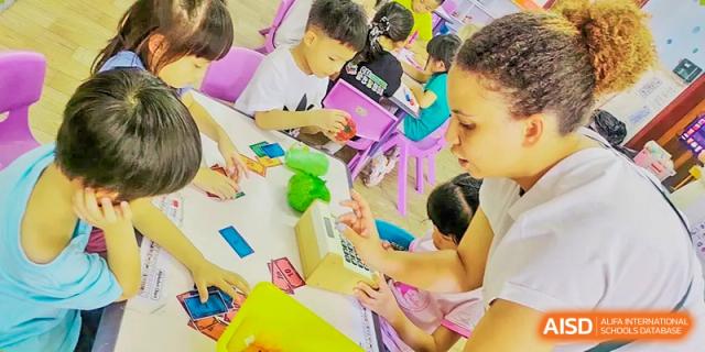 Young students at QSI International School of Zhuhai participate in a colorful, hands-on activity at a pink table.