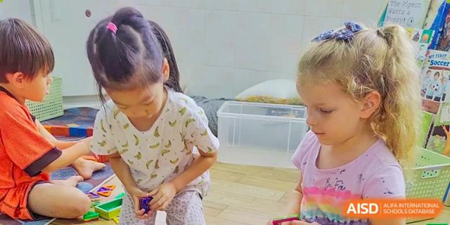 Close-up of young students from QSI International School of Zhuhai participating in a hands-on activity in an indoor play or classroom area.