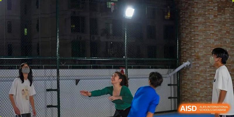 Two female teachers or staff members from QSI International School of Zhuhai engage in an outdoor activity at night, possibly a sports practice.