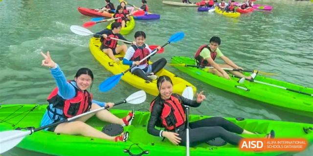 Students from QSI International School of Zhuhai in life jackets happily kayaking or canoeing on the water during an outdoor adventure trip.