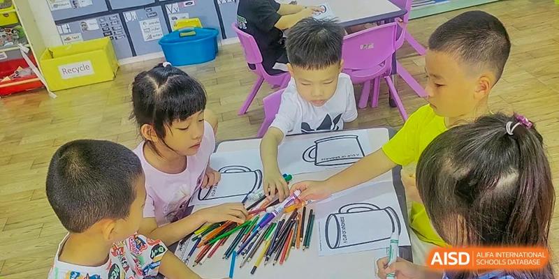 Young students at QSI International School of Zhuhai color a drawing together at a table with a large set of colored pencils.