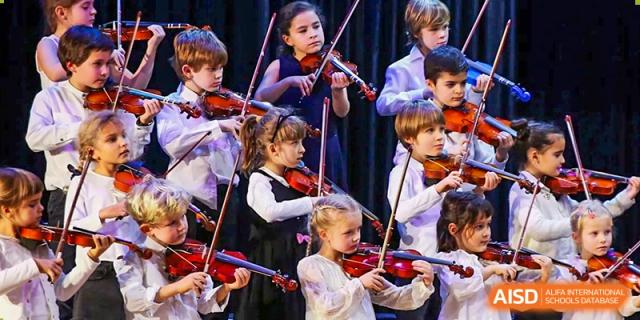 Young students from QSI International School of Zhuhai perform an orchestra concert, playing violins on stage.