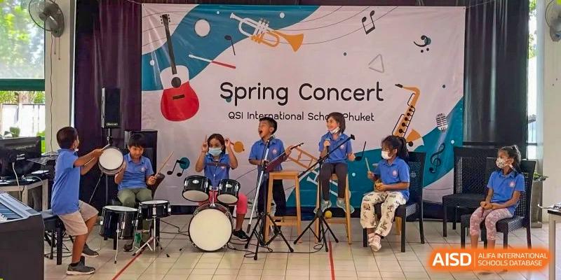 Students from QSI International School of Zhuhai performing with drums and a trumpet on stage at the Spring Concert.