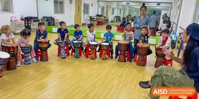 A group of elementary students at QSI International School of Zhuhai sits in a circle playing African drums during a music class.