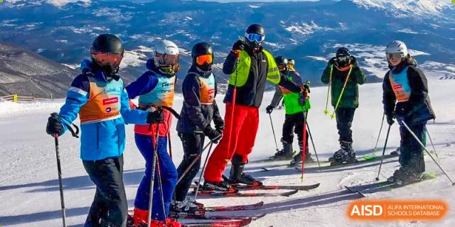 A group of students from QSI International School of Zhuhai in ski gear stands on a snowy mountain, participating in a winter sports trip.