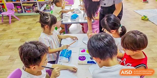 Elementary students at QSI International School of Zhuhai collaborate on an art project, drawing and painting at a table.