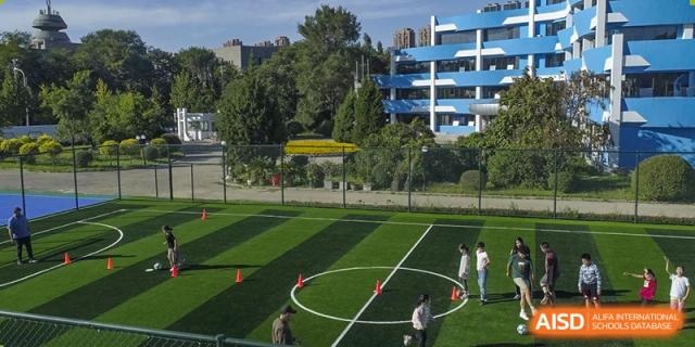 Outdoor view of the QSI International School of Zhuhai sports field and track with students participating in a drill or practice session.