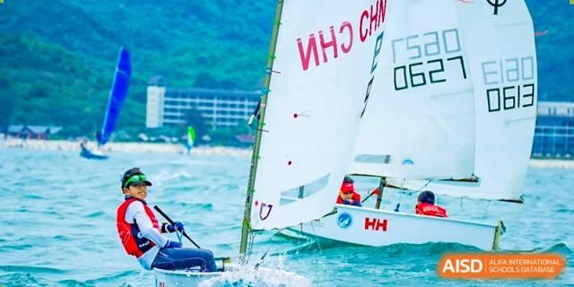 A small sailboat with the Chinese flag is sailing on the water as part of a sailing program at QSI International School of Zhuhai.