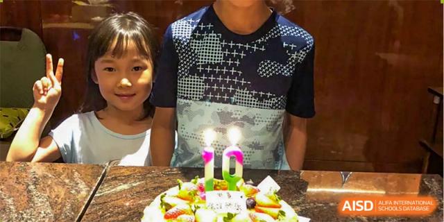 A student at QSI International School of Zhuhai celebrates a birthday with a cake, candles, and fruit.